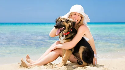 Donna sorridente con cappello bianco abbraccia cane sulla spiaggia