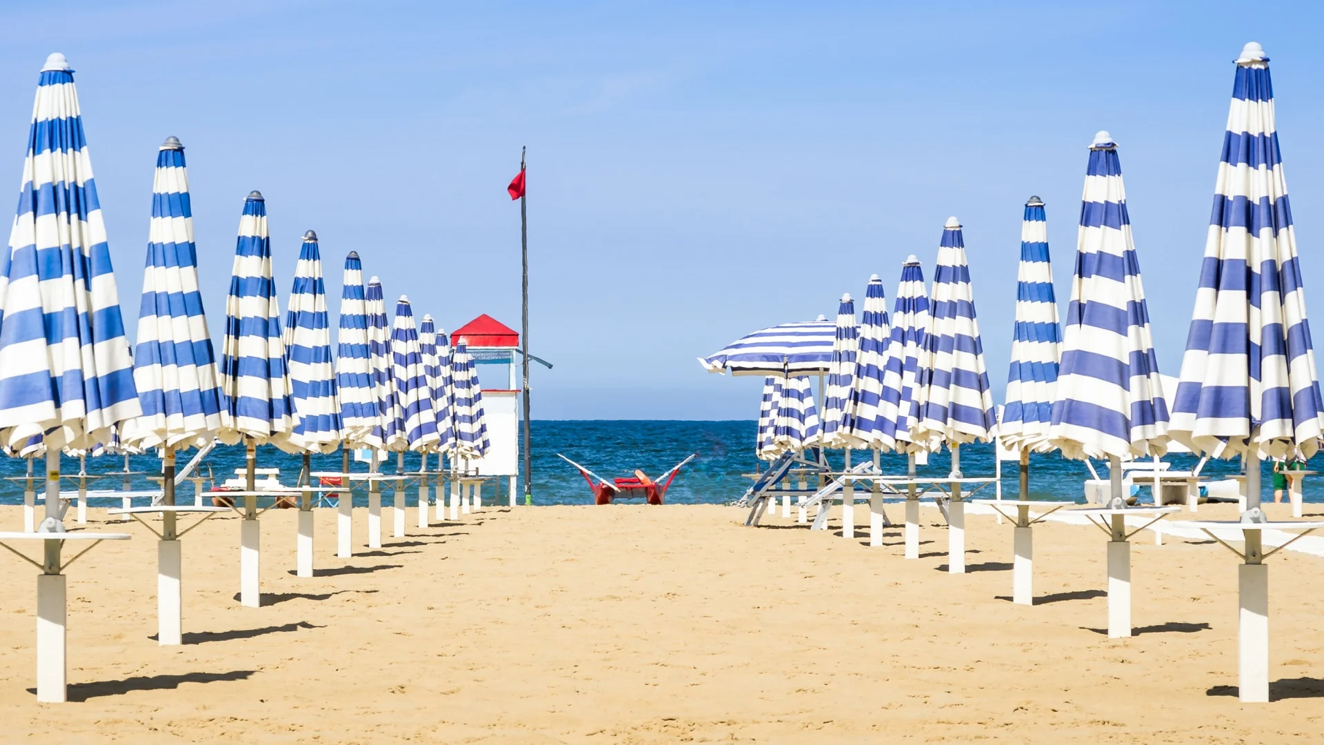 Ombrelloni blu e bianchi chiusi su una spiaggia sabbiosa con il mare sullo sfondo