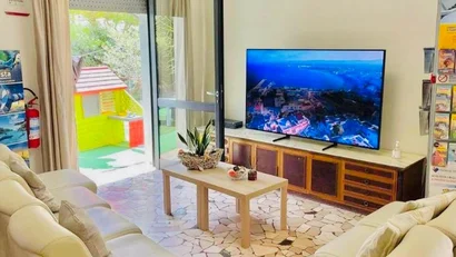 Soggiorno con divani beige, tavolino, TV e porta finestra aperta