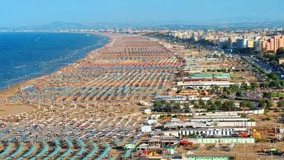 Vista aerea di una lunga spiaggia affollata con ombrelloni colorati e ville vicino al mare