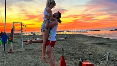 Coppia sulla spiaggia al tramonto, uomo solleva donna sorridente