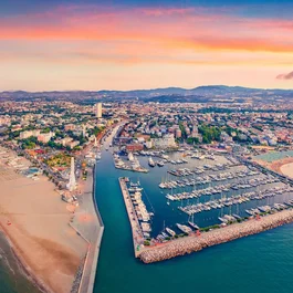 Veduta aerea del porto e della spiaggia al tramonto con la città e le montagne sullo sfondo