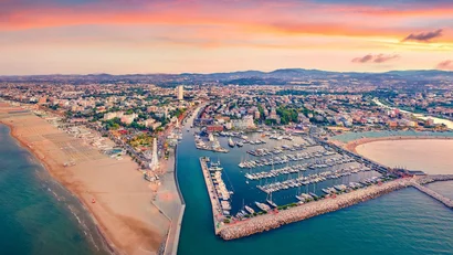 Veduta aerea del porto e della spiaggia al tramonto con la città e le montagne sullo sfondo