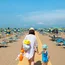 Donna e bambina che camminano su una spiaggia con ombrelloni blu e gialli