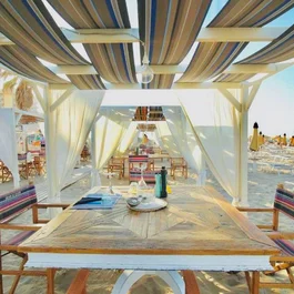 Area pranzo coperta sulla spiaggia con sedie e tavoli di legno